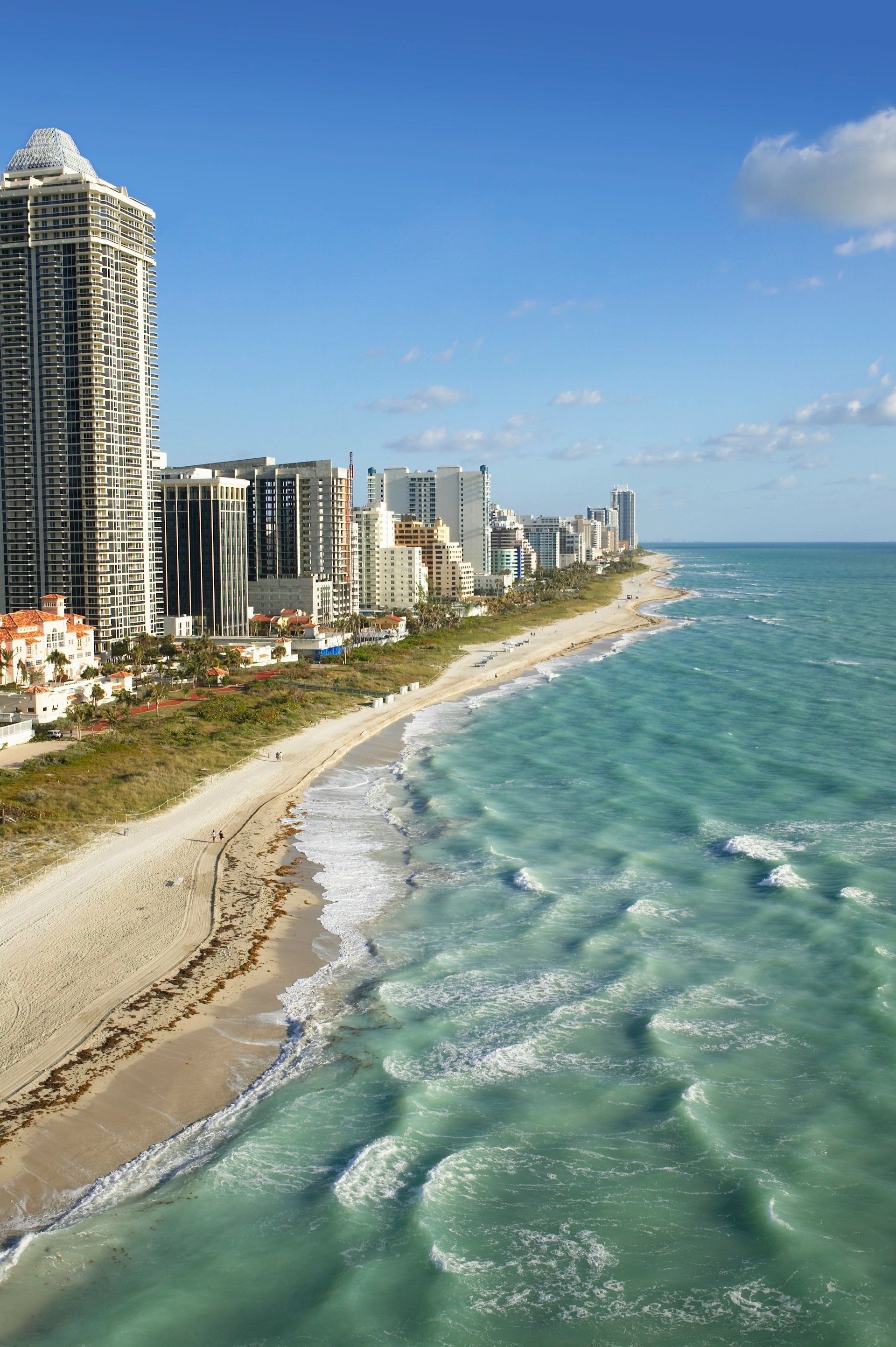 Beachfront with high-rise buildings, turquoise water, and blue sky.
