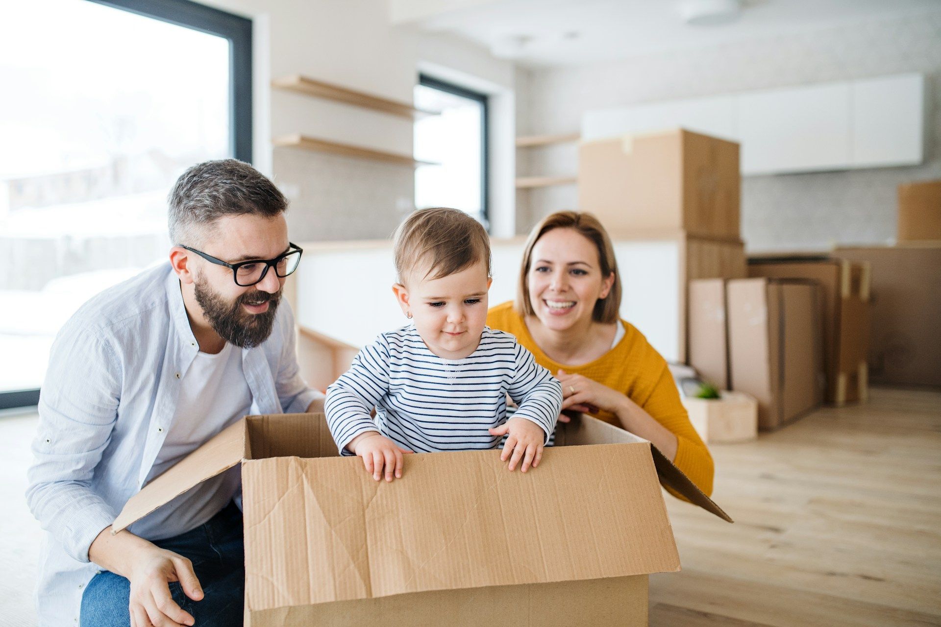 Family playing with child in a moving box in a new home; smiling.