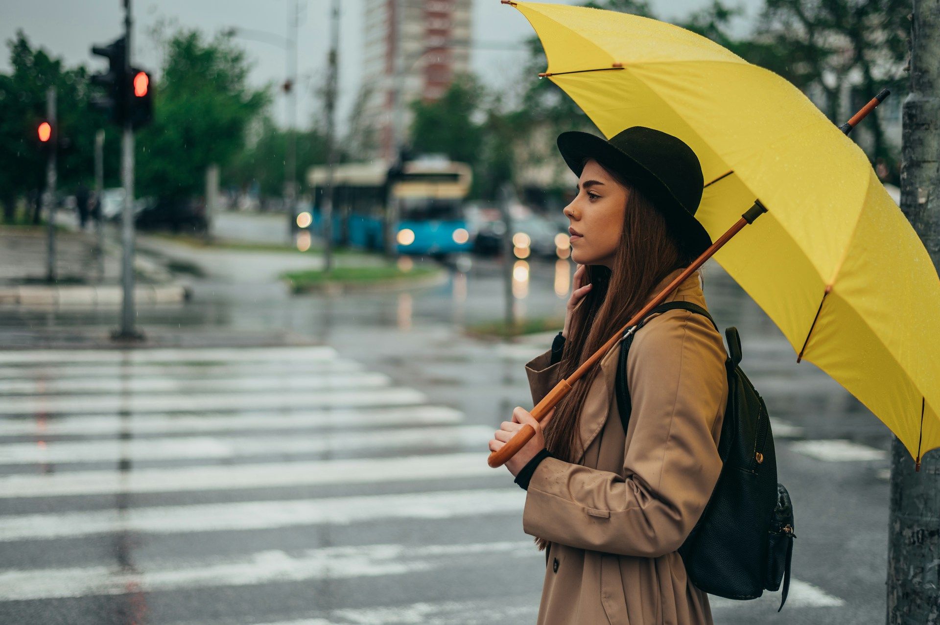 Woman with yellow umbrella waits at a crosswalk in the rain.