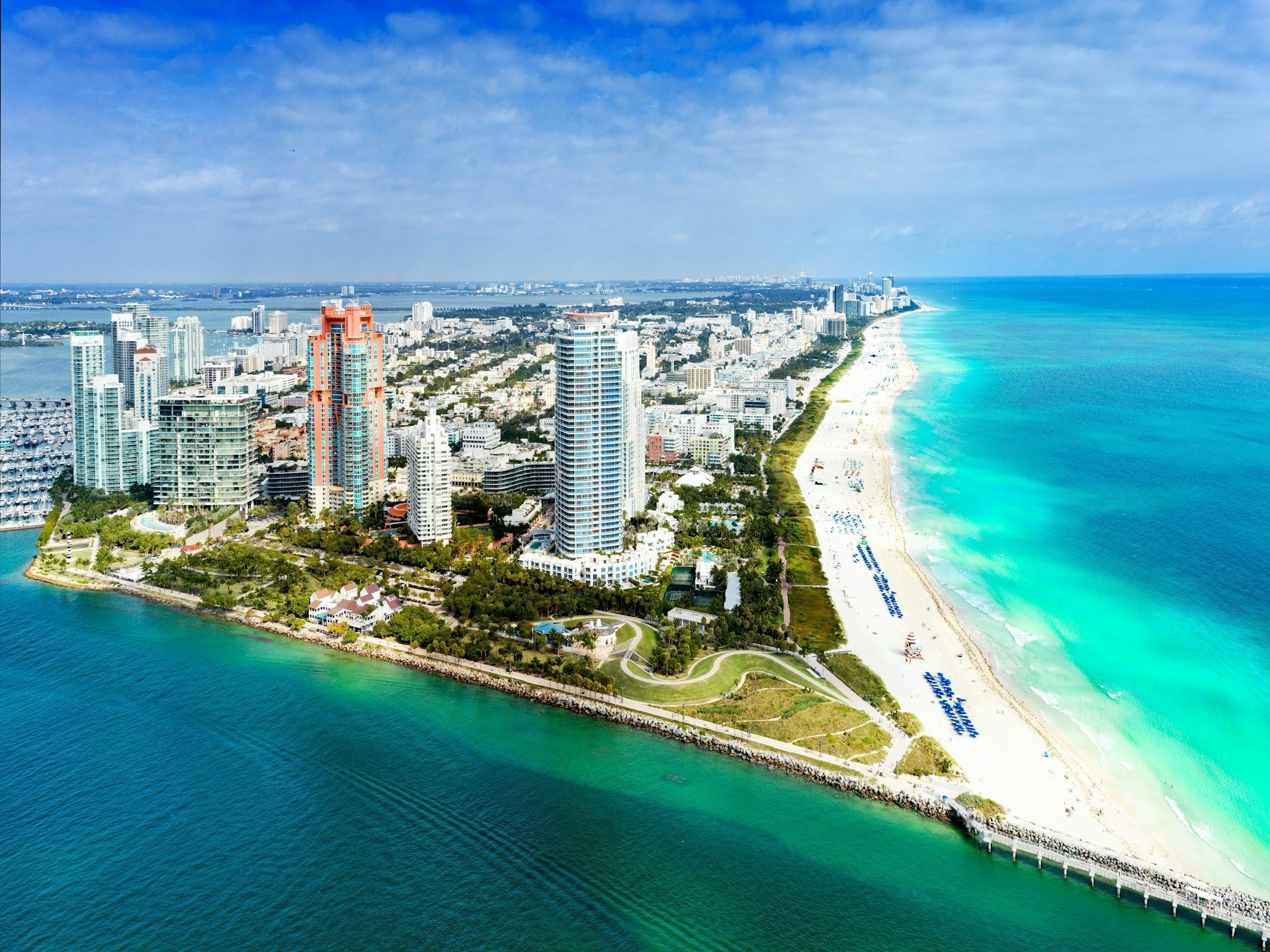 Aerial view of Miami Beach, Florida, with turquoise ocean, sandy shore, and high-rise buildings under a clear blue sky.
