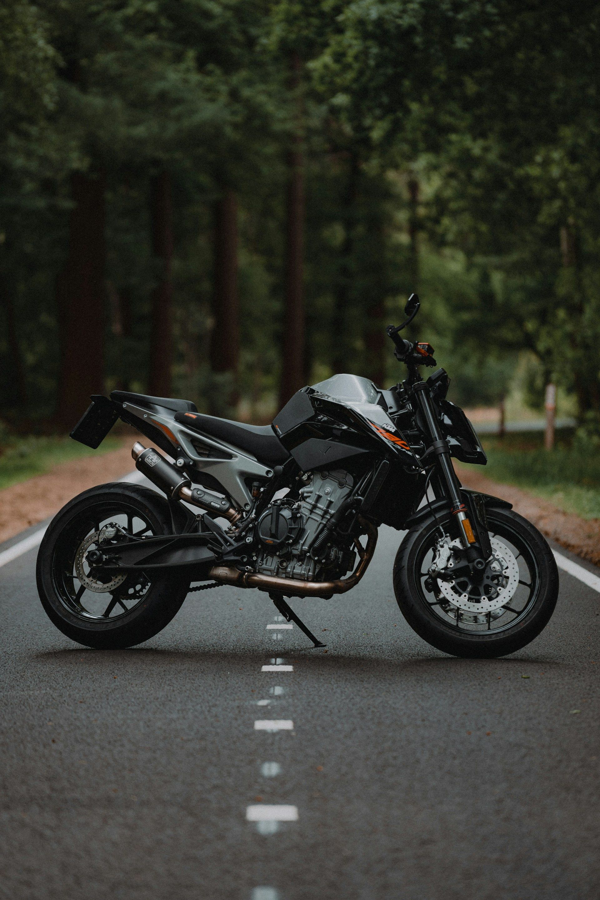 Black motorcycle parked on a paved road, trees in the background.
