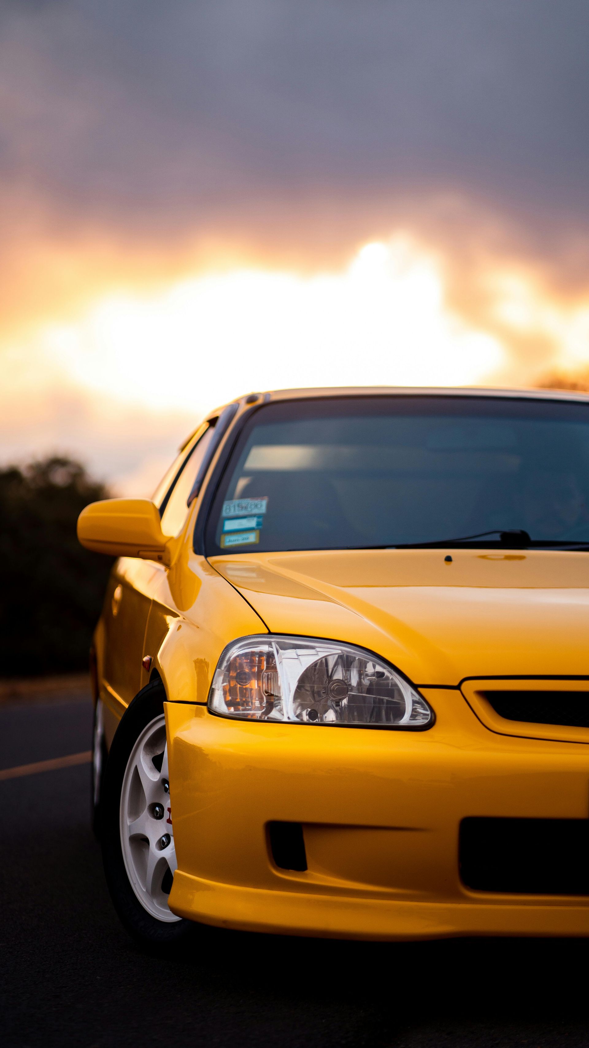 Yellow Honda Civic parked with a sunset in the background.