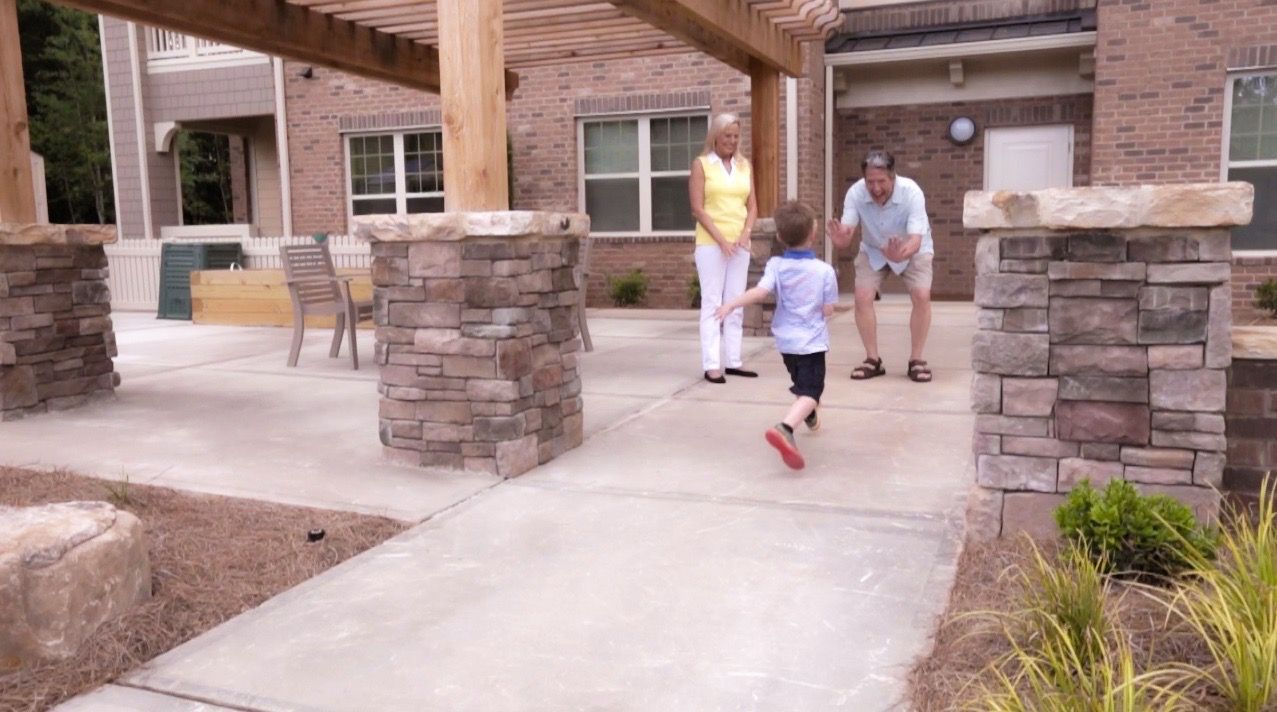 Family with a child playing outdoors near an apartment building entrance under a wooden pergola.
