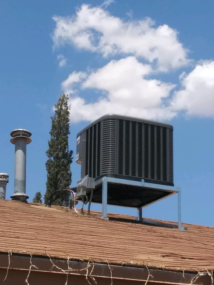 Rooftop air conditioning unit on a brown roof, with a tall tree and blue sky with clouds.