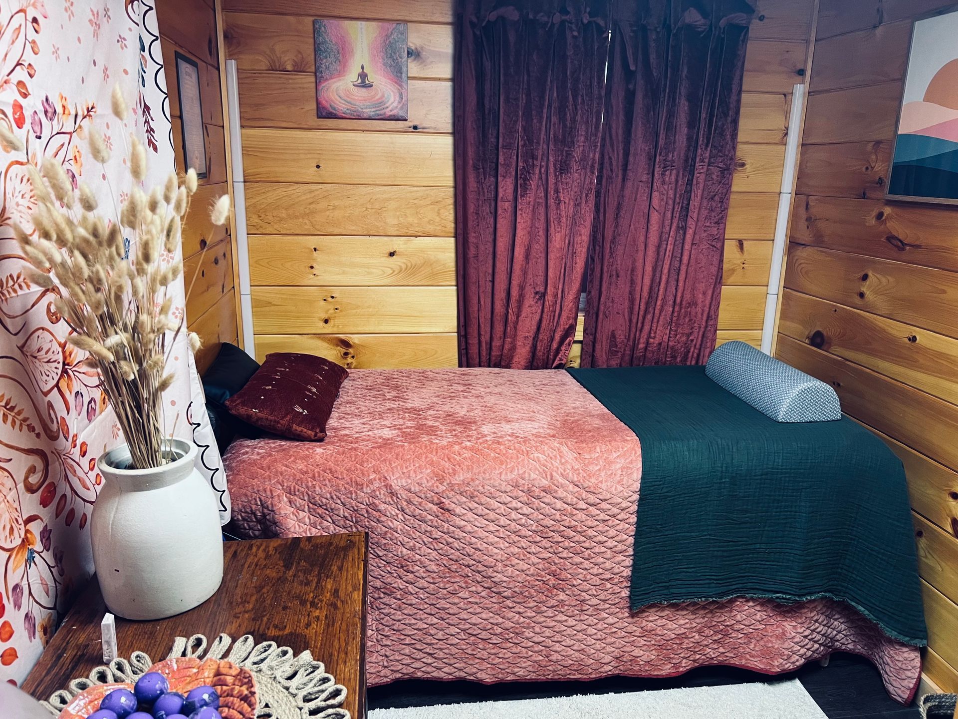 Cozy wooden bedroom with two beds, burgundy curtains, and a vase of dried flowers