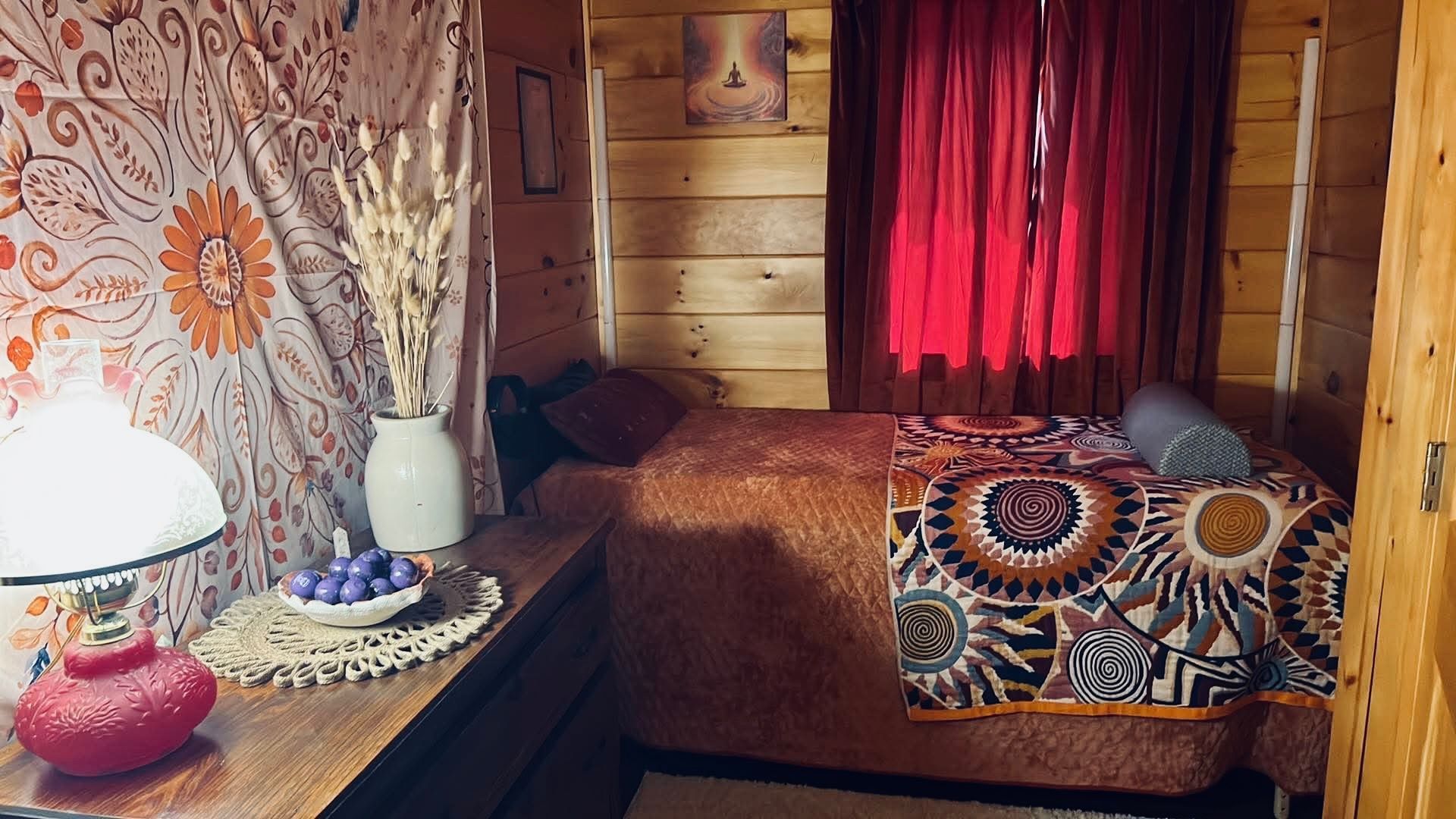 Cozy wood-paneled room with red curtains, patterned sofa, and a table lamp by a tapestry wall