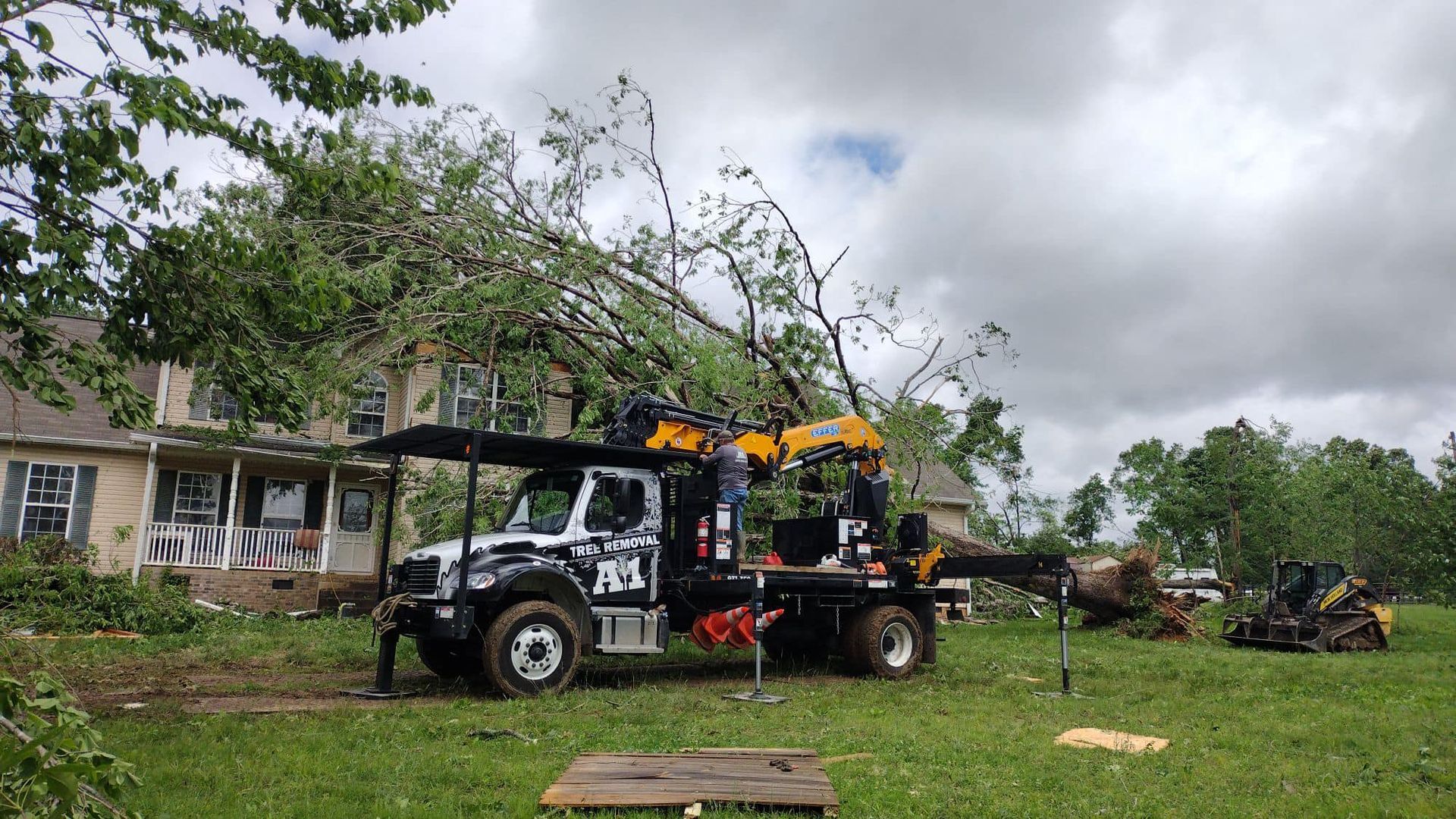 White utility truck with orange equipment in a grassy yard near a house under cloudy skies