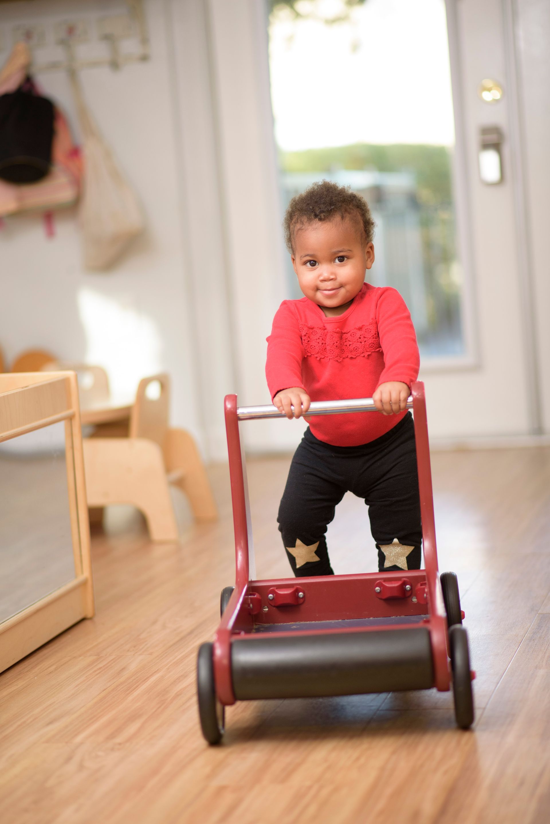 Toddler in a red sweater pushing a red toy walker indoors.