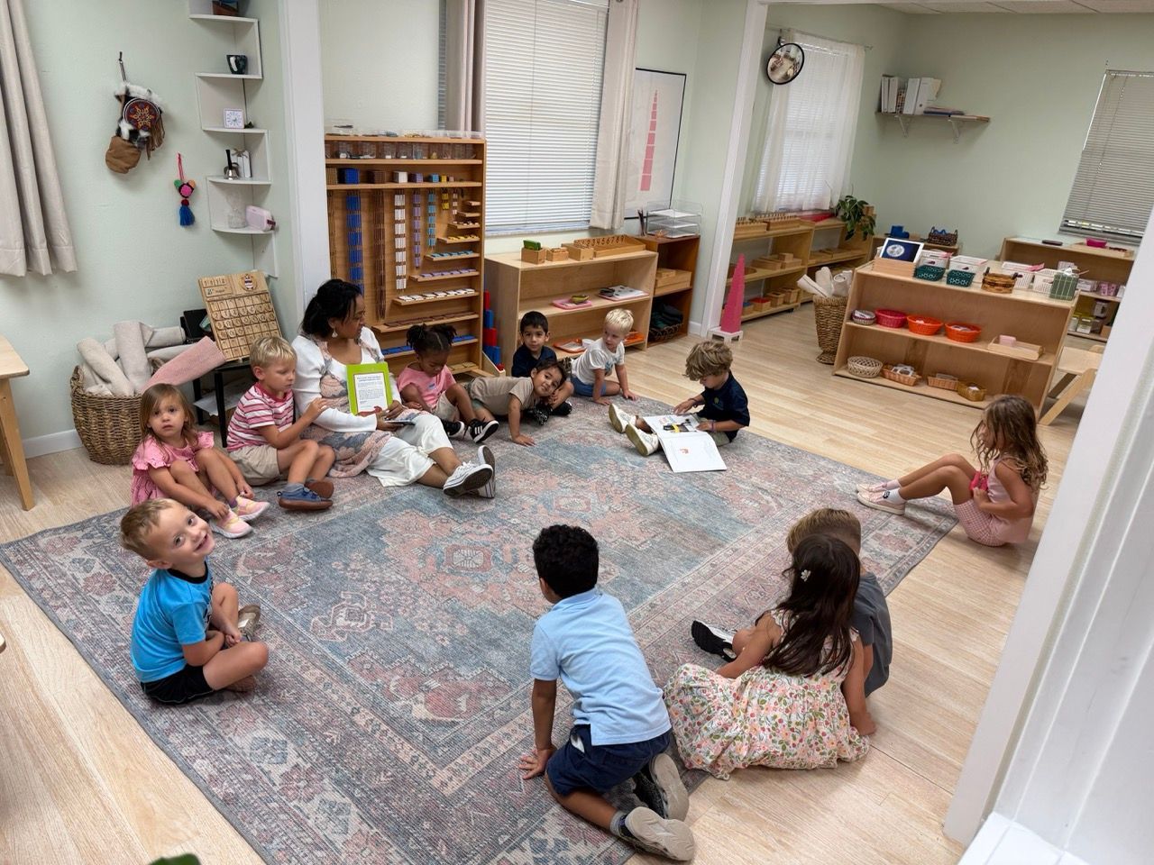Children sitting in a classroom circle with materials and books on shelves in the background