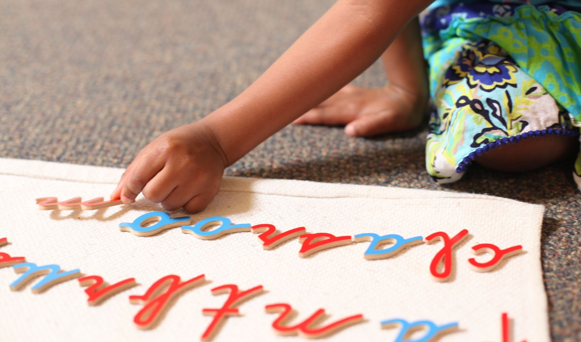 Child’s hand arranging moveable alphabet letters on a white mat during a learning activity