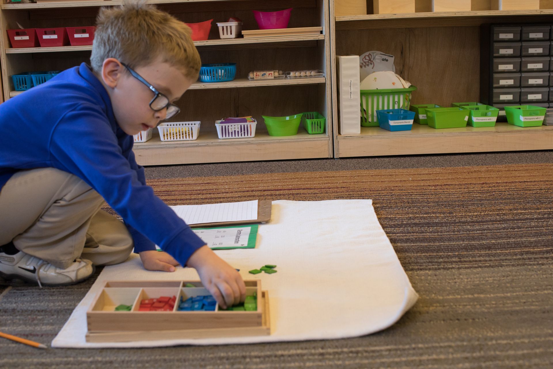 Child kneeling on classroom carpet, working with the stamp game
