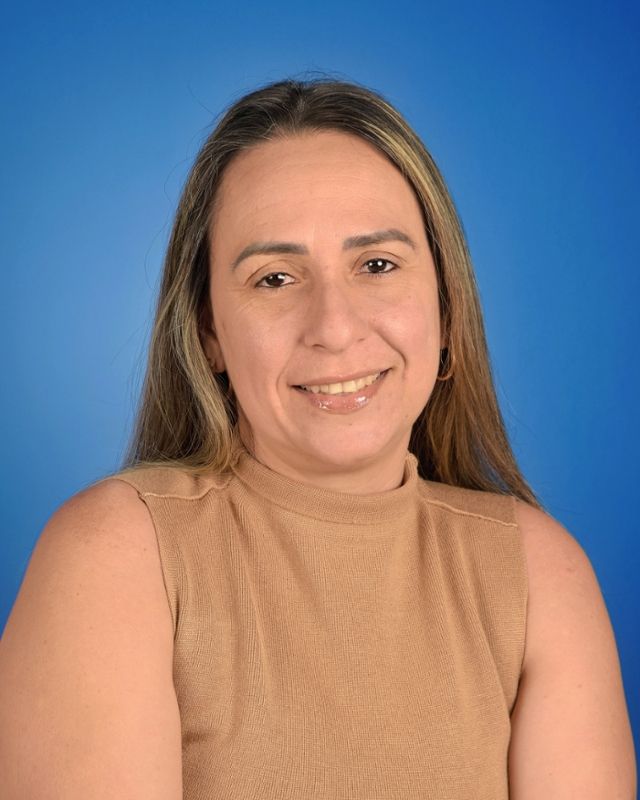Portrait of a smiling person in a tan sleeveless top against a blue background