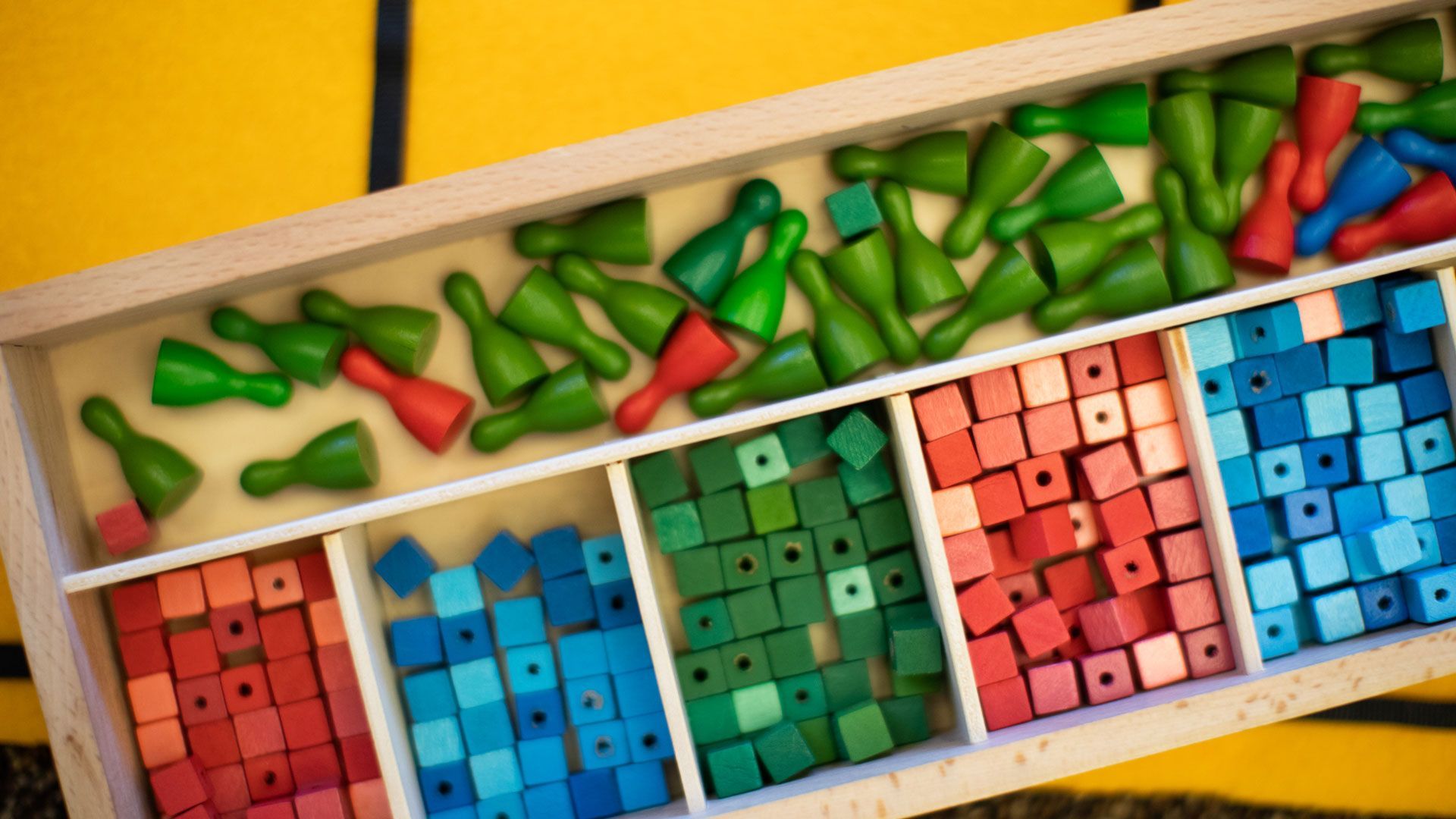 Overhead view of a game tray with colorful beans and three compartments of red, blue, and pink cubes