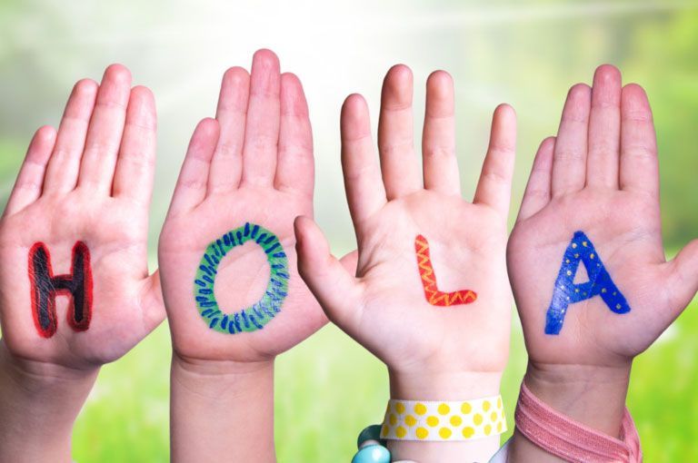 Hands spelling “HOLA” with colorful letters on palms against a soft green background