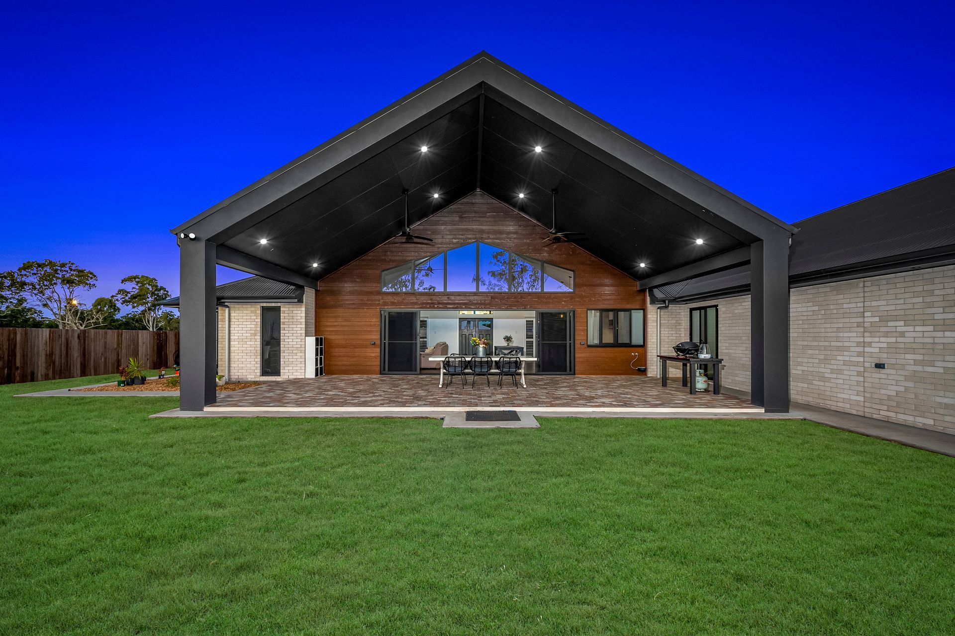 Modern backyard with covered patio, brick house exterior, and a green lawn at dusk