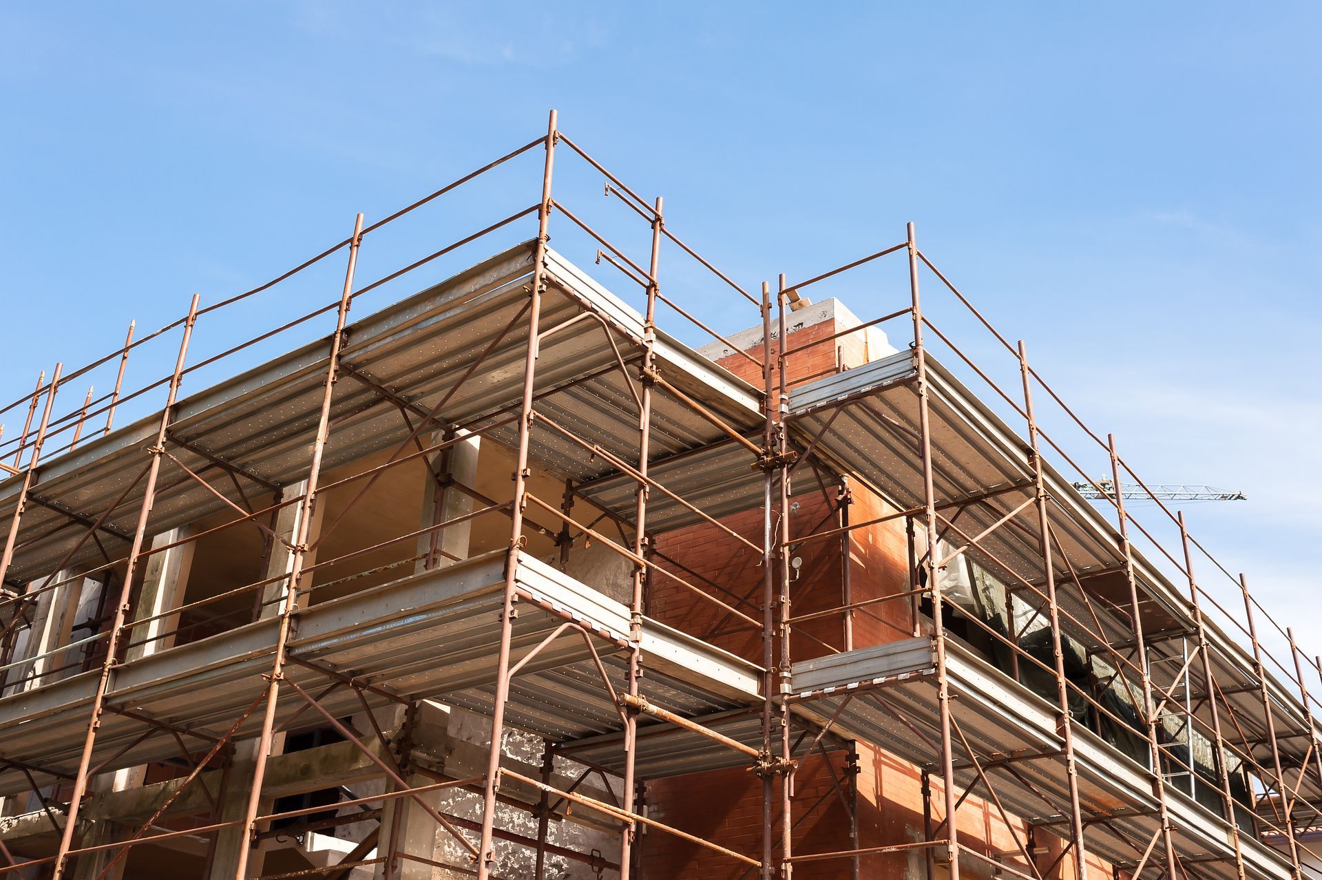 Scaffolding around a multi-story building under construction against a blue sky