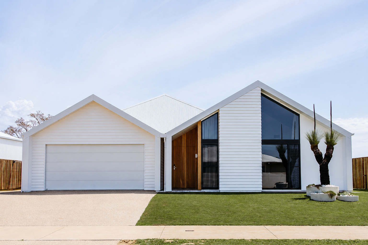 Modern white house with a garage, large windows, and a front lawn under a blue sky