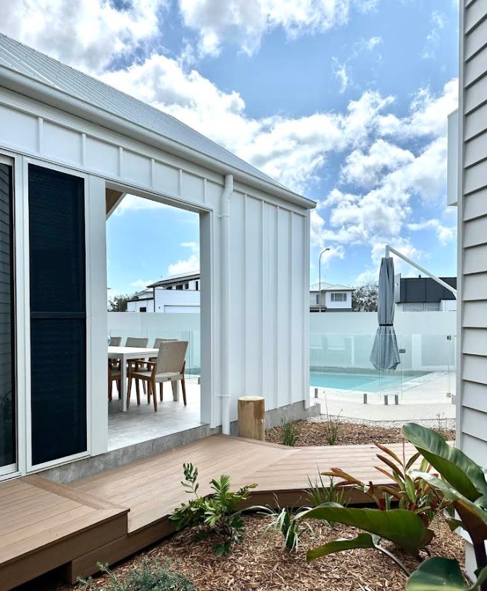Modern seaside patio with wooden deck, white cottage, sliding door, pool, and ocean view