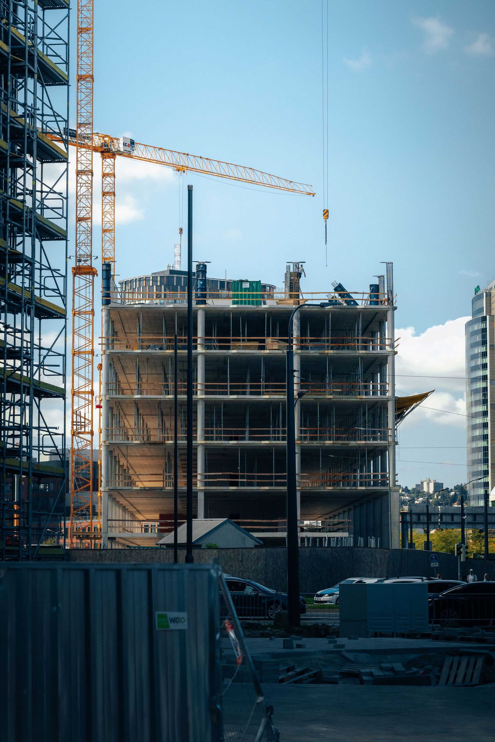 Construction site with a multi-story building under construction and a yellow crane against a blue sky