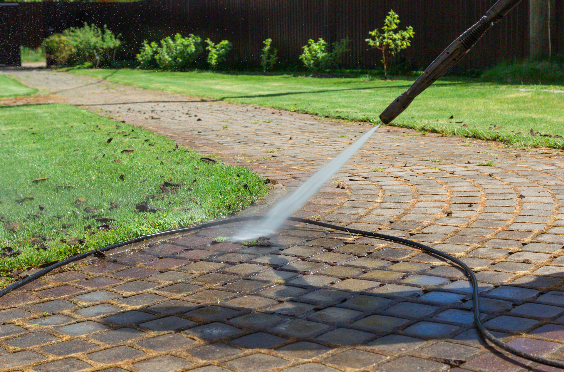 A person is using a high pressure washer to clean a brick walkway.