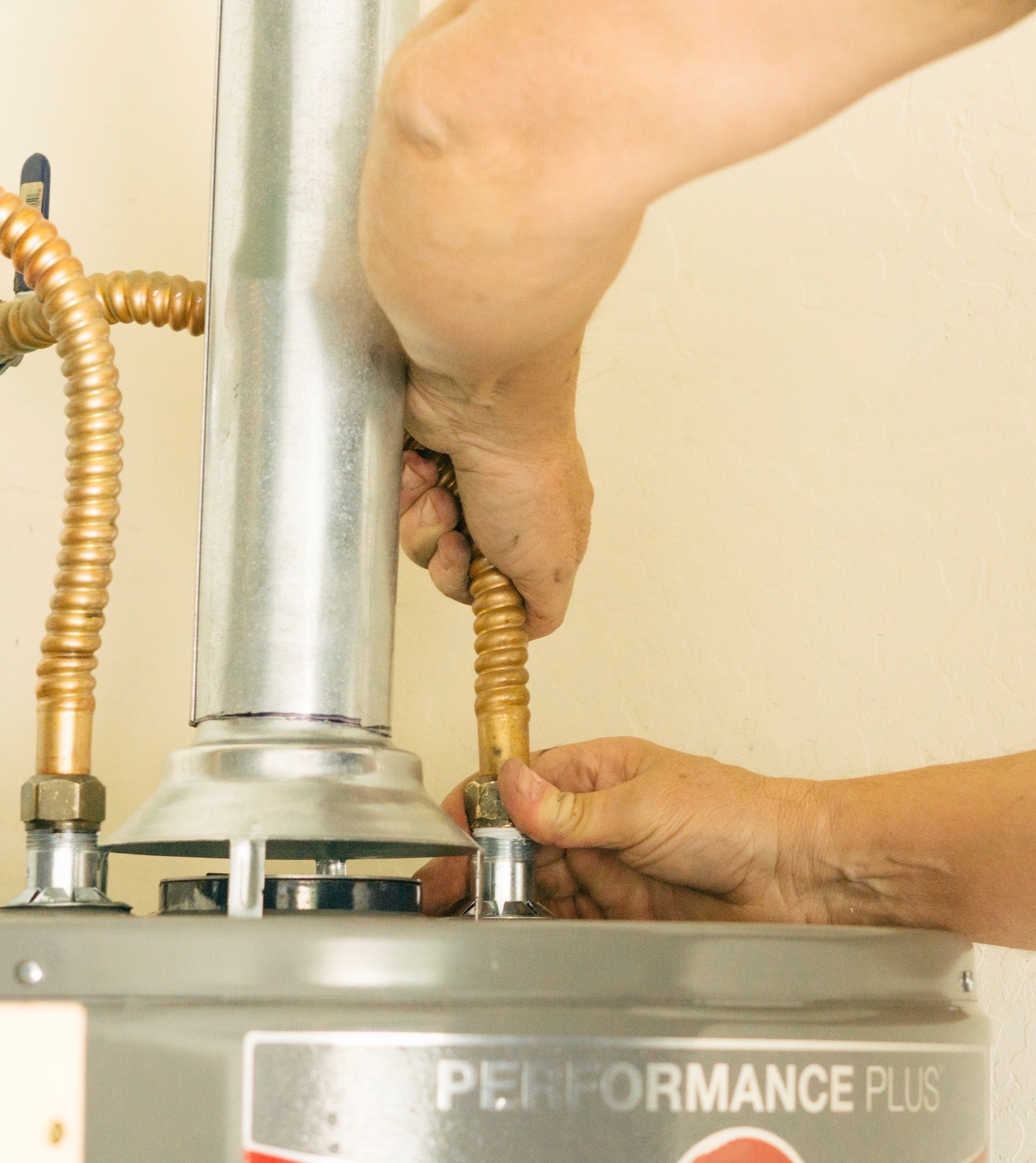 Person attaching a brass hose to a water heater; indoor setting.