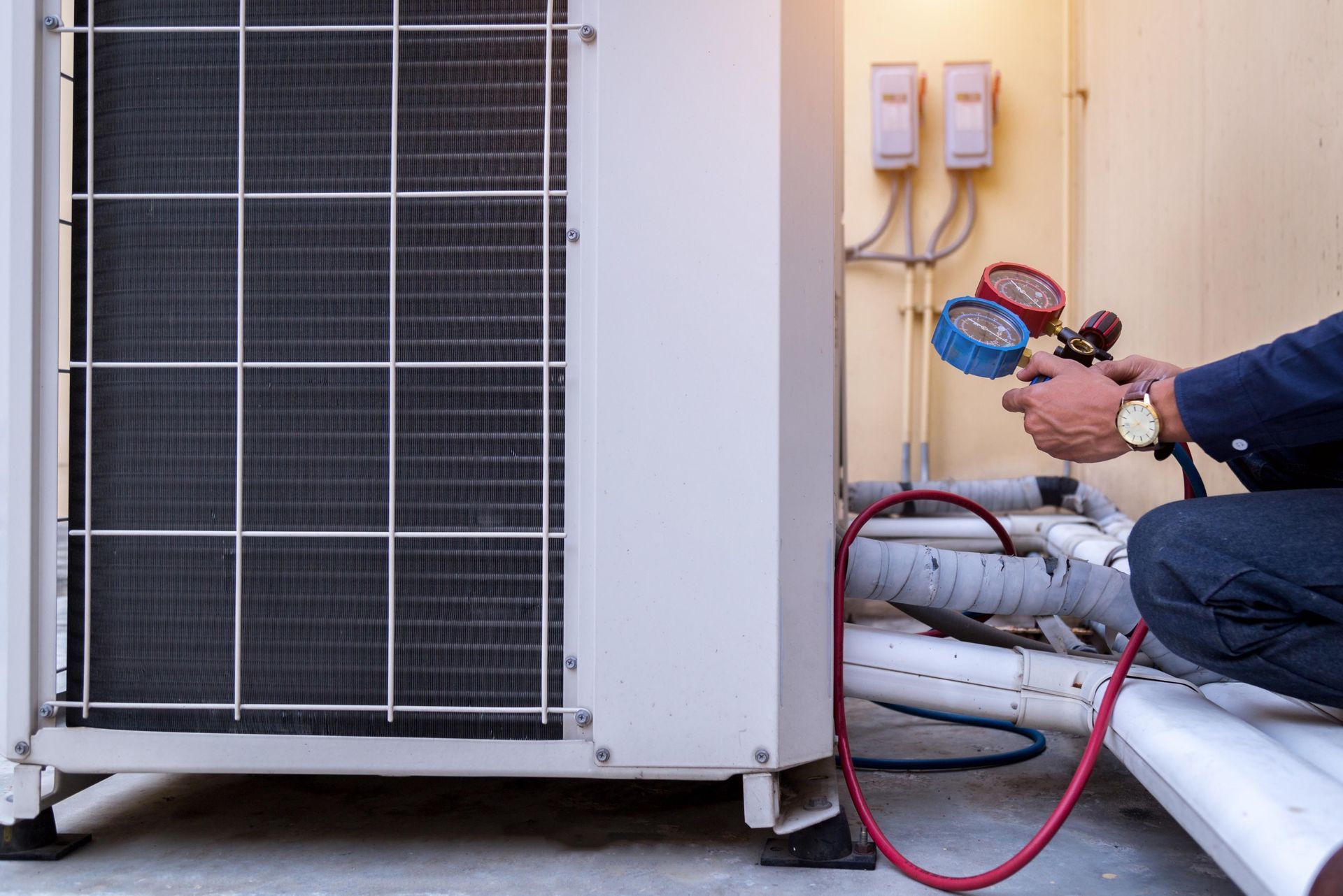 A technician servicing an outdoor air conditioning unit, using gauges to check pressure.