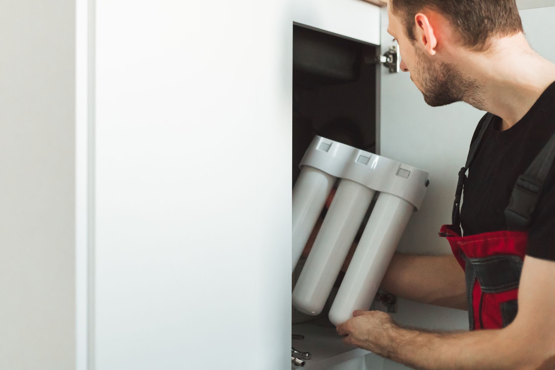 Man installing water filter system under a white cabinet.