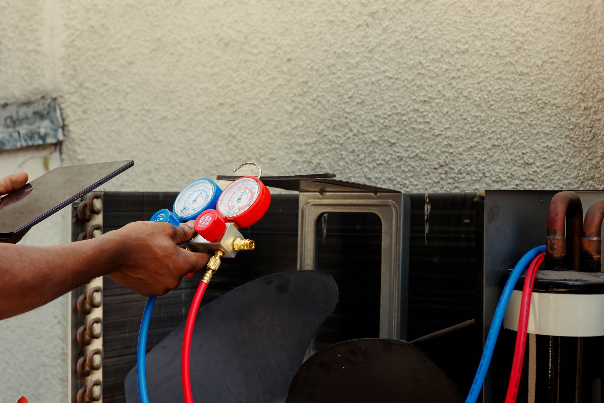 Person connecting gauges to an air conditioning unit outside, reading pressure levels.