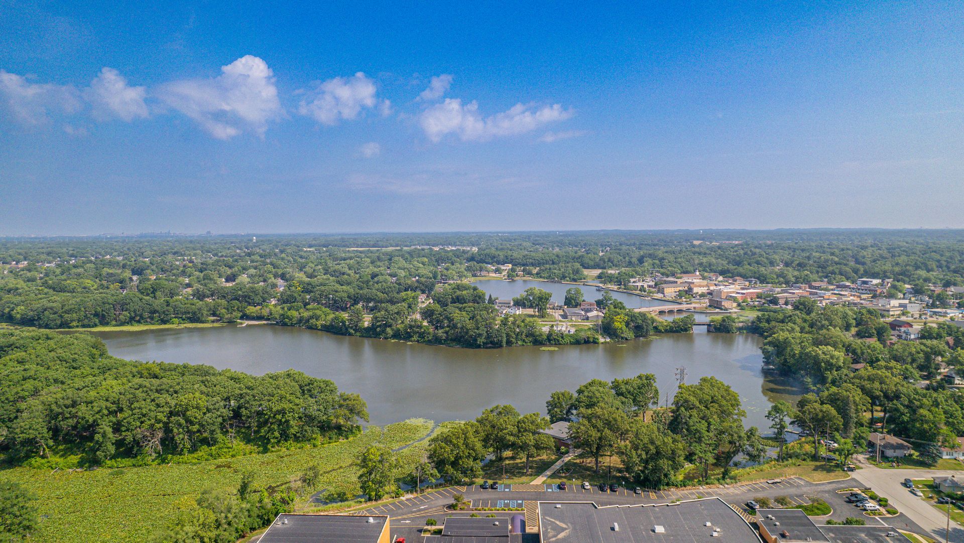 Aerial view of a lake surrounded by trees and a town under a blue sky.