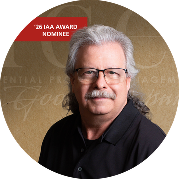 Man with gray hair and glasses, wearing a black shirt, looking at the viewer.