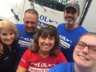 Five people smiling for a selfie in front of a moving truck; they wear blue and red LOL Transport & Moving shirts.