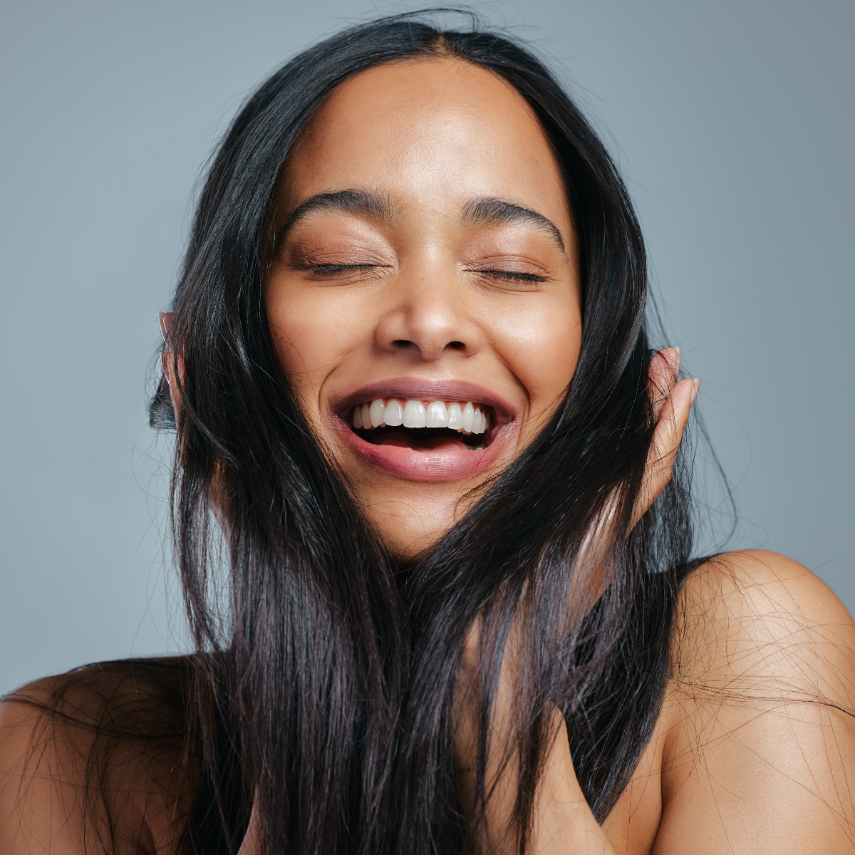 A woman with long black hair is smiling with her eyes closed.