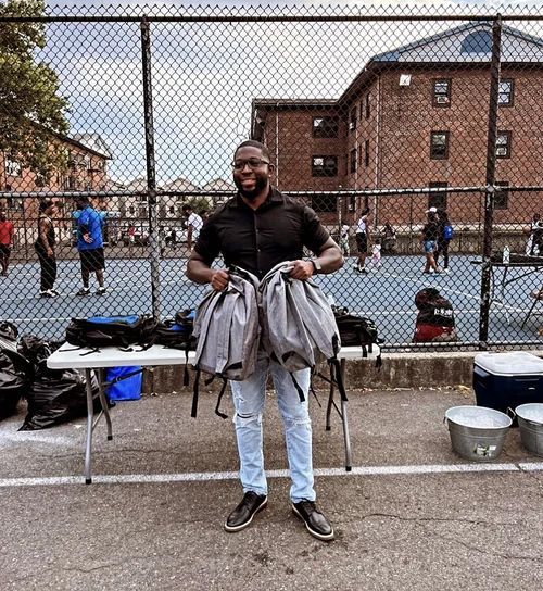 Man holding a bags near a fenced basketball court Man holding a bags near a fenced basketball court