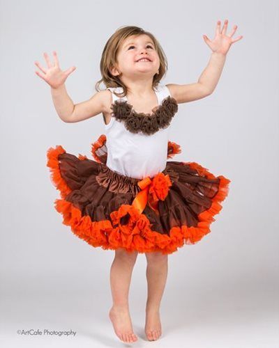 Girl wearing a turkey-themed tutu, jumping with arms raised and a happy expression.