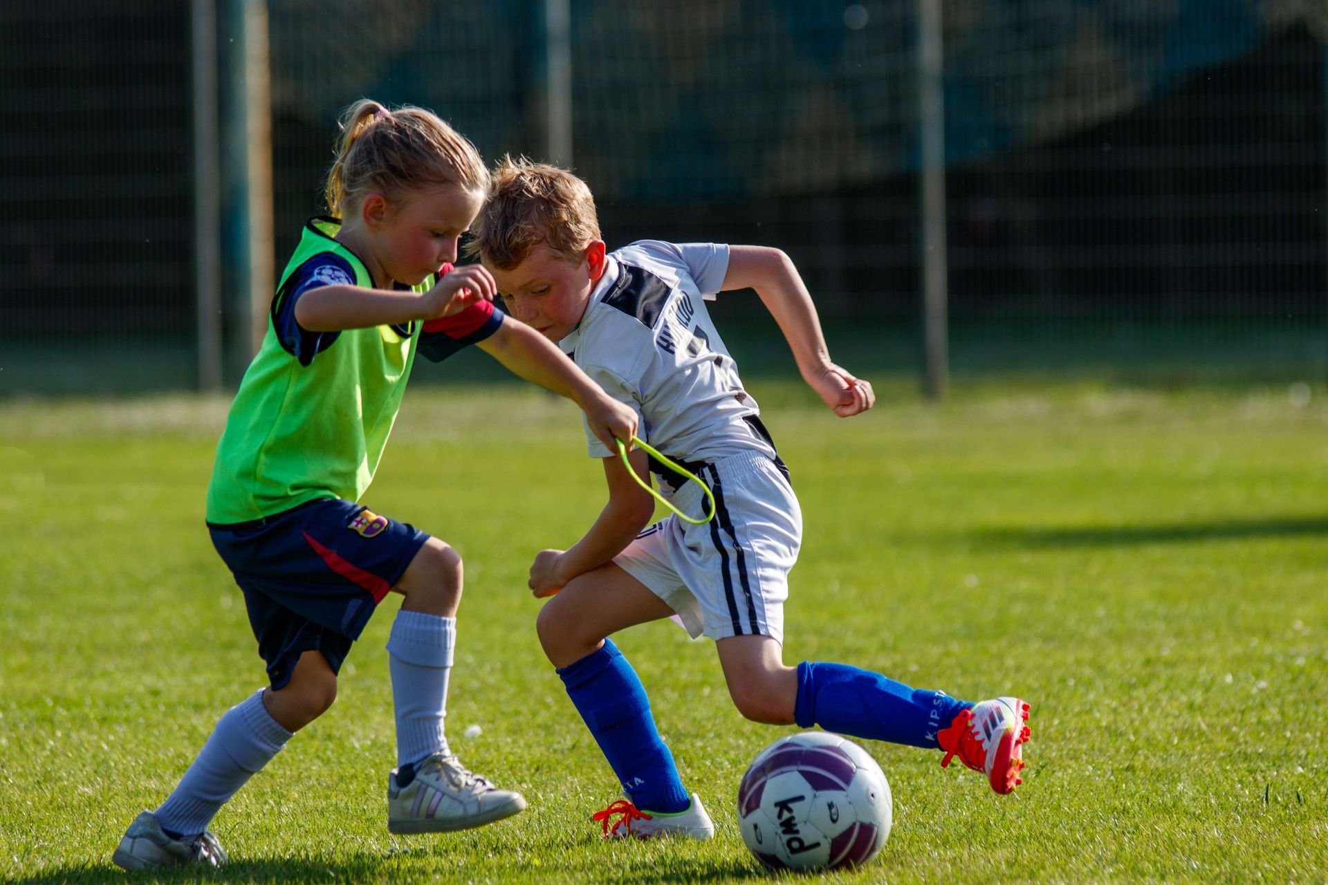 Two children in soccer uniforms contest the ball on a grassy field outdoors.