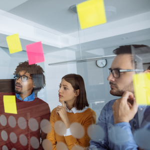 Team collaborating in an office, looking at notes on a glass wall with sticky notes.