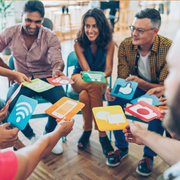 People in a circle holding colorful social media icon cards, smiling in a casual meeting room