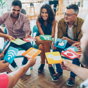 People in a circle holding colorful social media icon cards, smiling in a casual meeting room