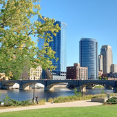 Riverside skyline with modern glass towers, arched bridge, and trees under a clear blue sky
