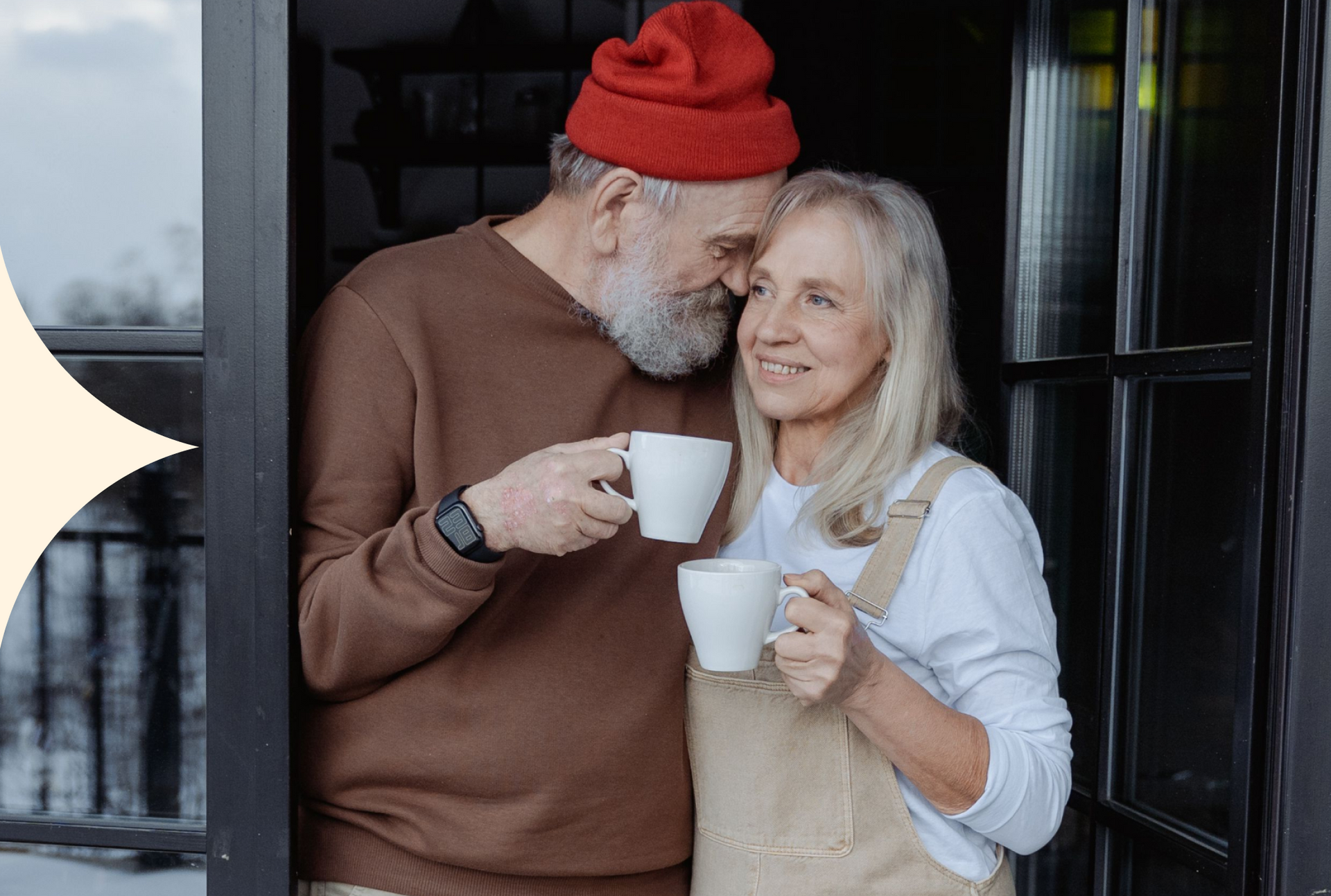 Two people sharing coffee on a porch, smiling warmly, one in a red hat and the other in a light apron.