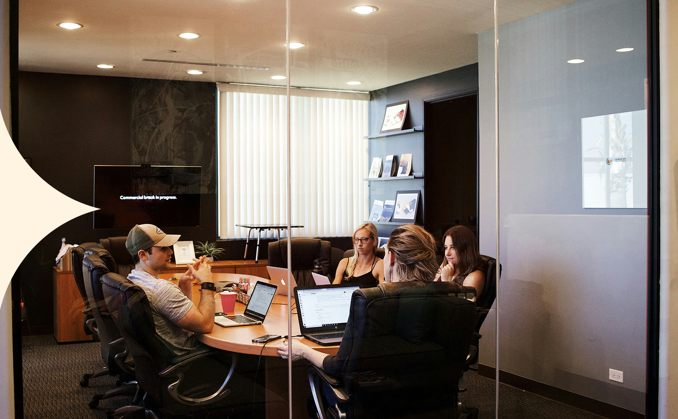 People seated around a conference table in a modern office meeting room, discussing papers and laptops.