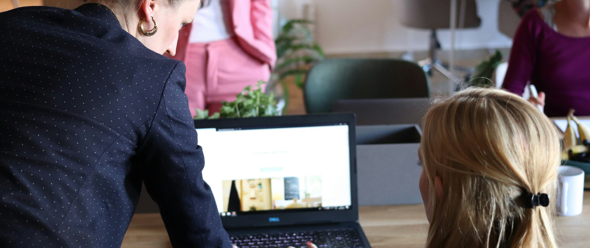 People gathered around a laptop in a meeting room, with one person standing and pointing at the screen.