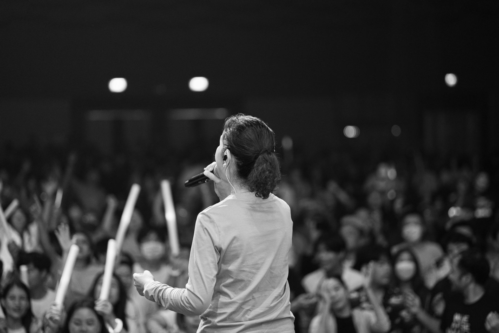Speaker on stage addressing a blurred crowd, holding a microphone in black-and-white scene