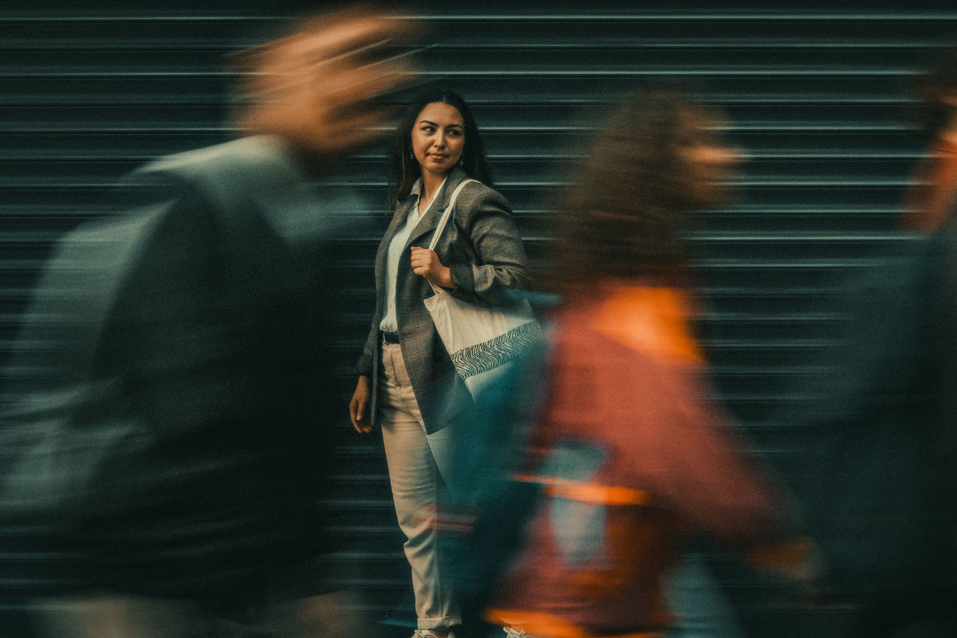 Woman standing on a city street as blurred pedestrians pass in front of her.