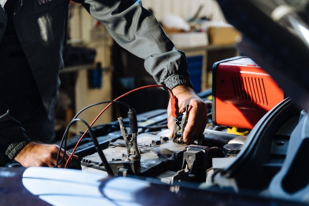 Mechanic Using Jumper Cables to Charge a Car Battery in a Garage — Mullumbimby Auto Electrical in Mullumbimby, NSW
