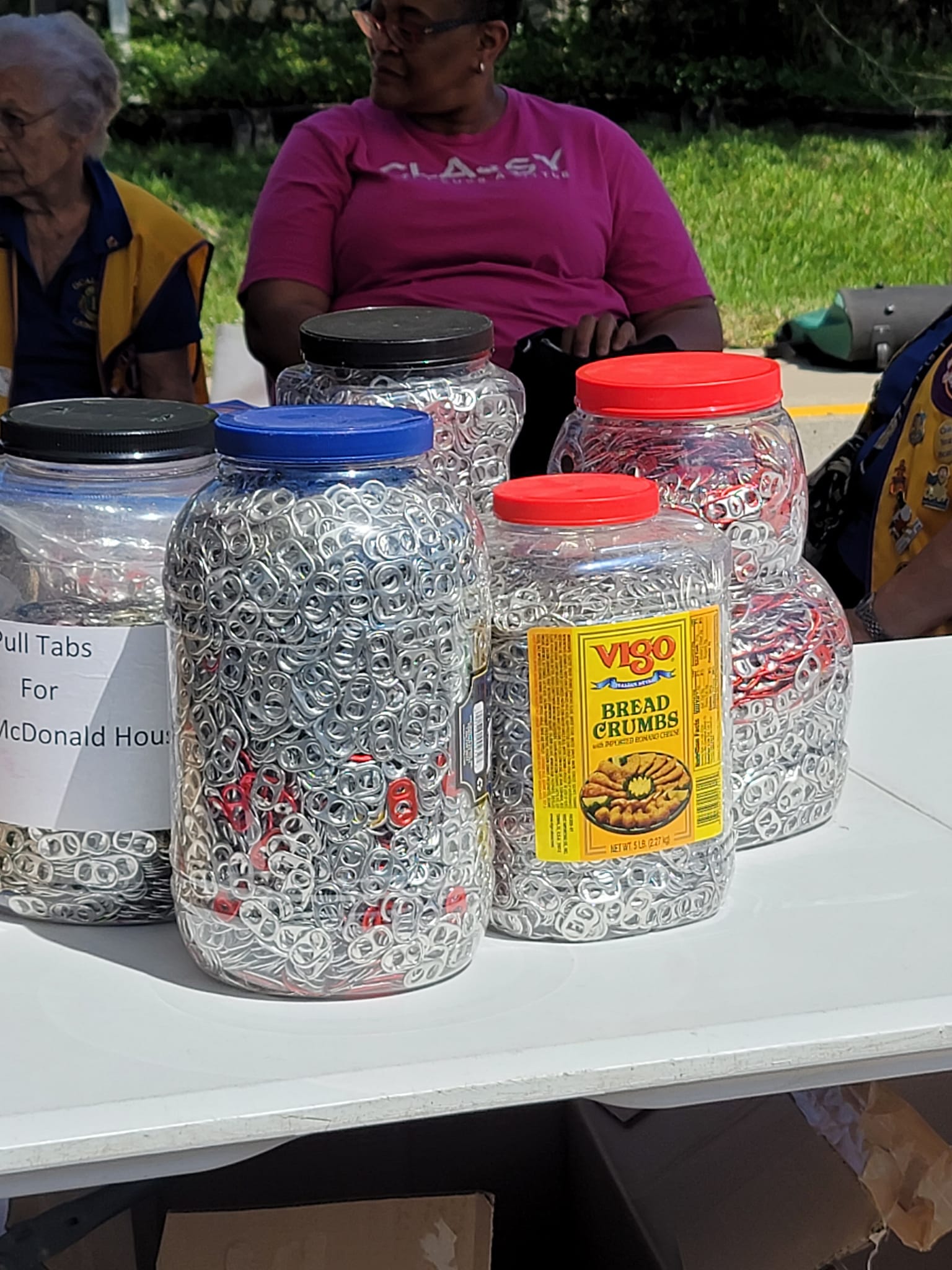 Jars of candy on a table, people in the background. Some jars have colorful lids.