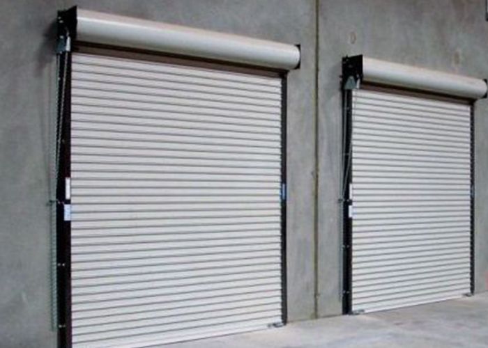 Dos puertas de garaje enrollables blancas cerradas sobre una pared de hormigón gris.
