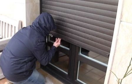 Persona ajustando una contraventana gris sobre una ventana con marco negro en el exterior de una casa.