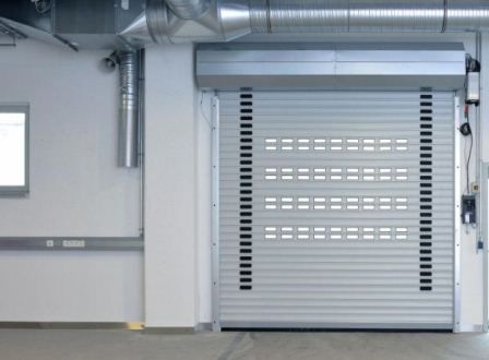 Garaje industrial con una puerta enrollable gris cerrada y conductos metálicos suspendidos en el interior de un almacén