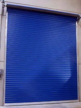 Una persiana metálica azul enrollable se cerraba en una abertura de pared beige.